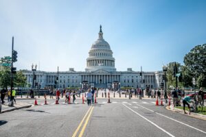 People walking and cycling near the US Capitol Building in Washington, D.C. on a sunny day.